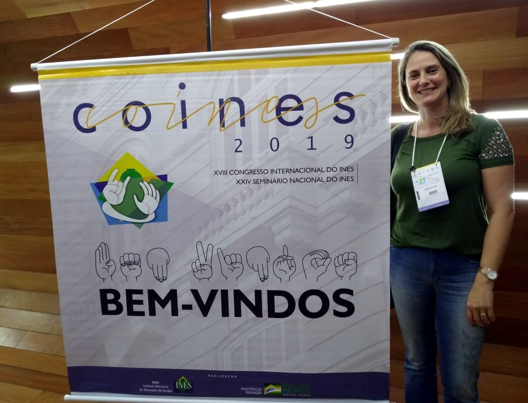 Fernanda Faucz ao lado de banner escrito: COINES 2019 Bem vindos