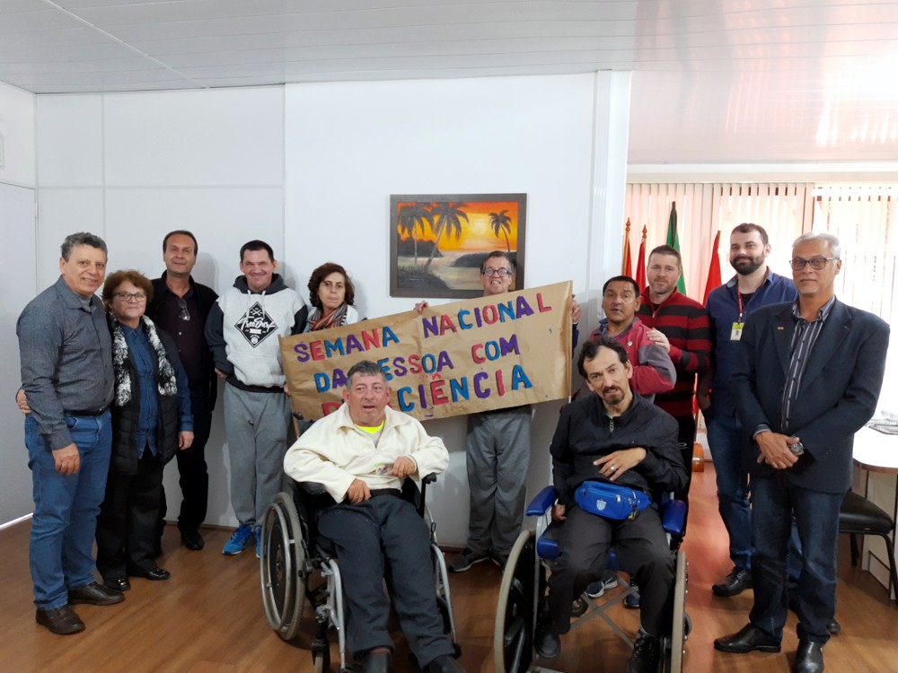 Grupo de educandos, professores e gestores da Fundação posam para foto. Dois cadeirantes ao centro e a faixa com a escrita "Semana Nacional da Pessoa com Deficiência"