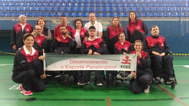 Na foto, os atletas de Bocha Paralímpica e técnico reunidos, segurando um cartão que diz 