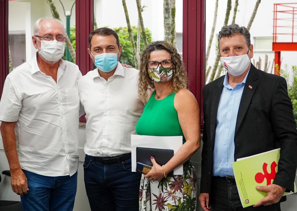 Quatro pessoas posam para foto em ambiente interno, ao fundo bandeira de Santa Catarina