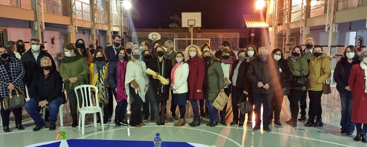 Ambiente externo, pátio de escola, cerca de vinte pessoas em pé posando para foto