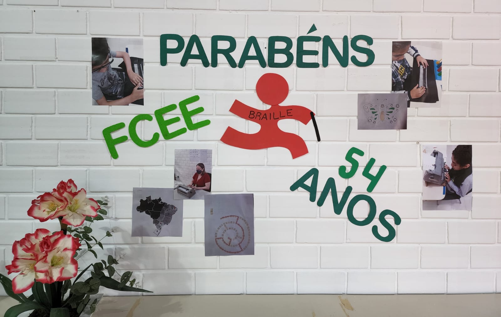 Mural branco com texto Parabéns FCEE 54 anos - Braille e imagens