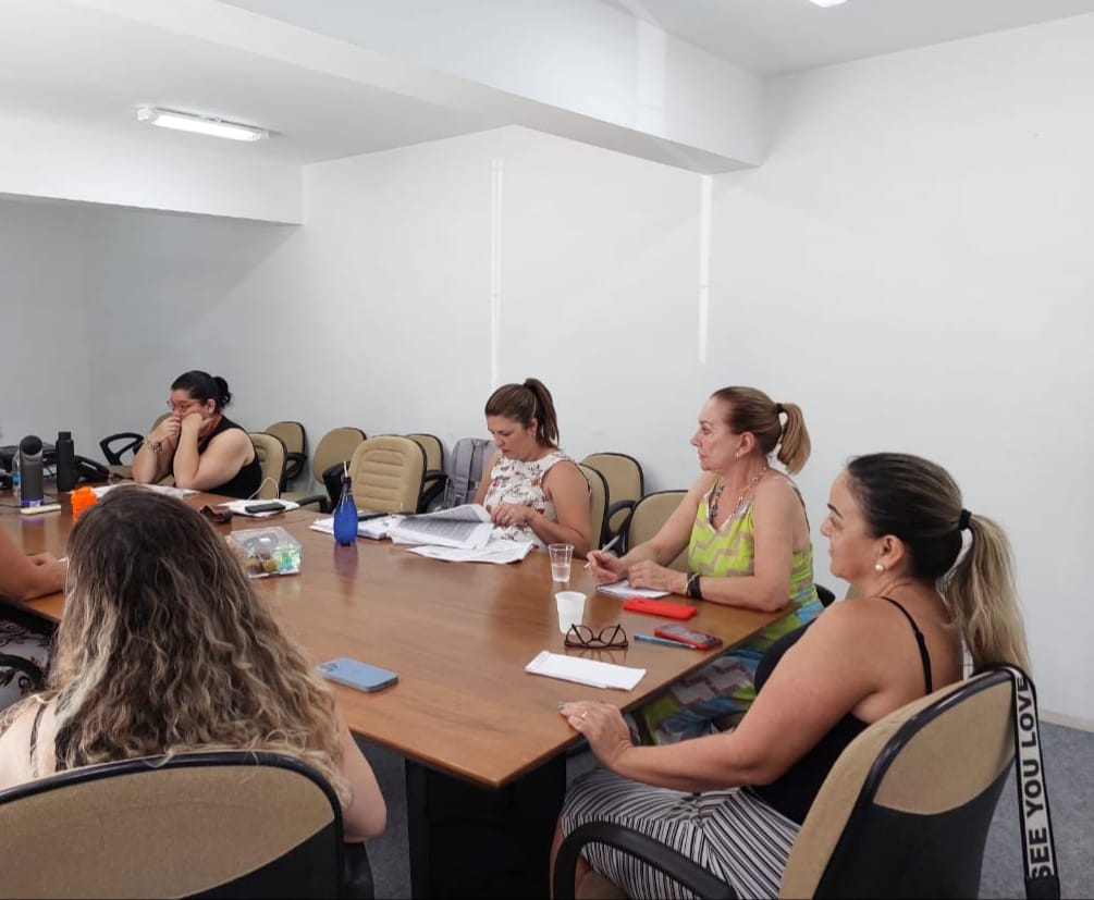 Imagem mostra cinco mulheres sentadas ao redor de uma mesa em reunião