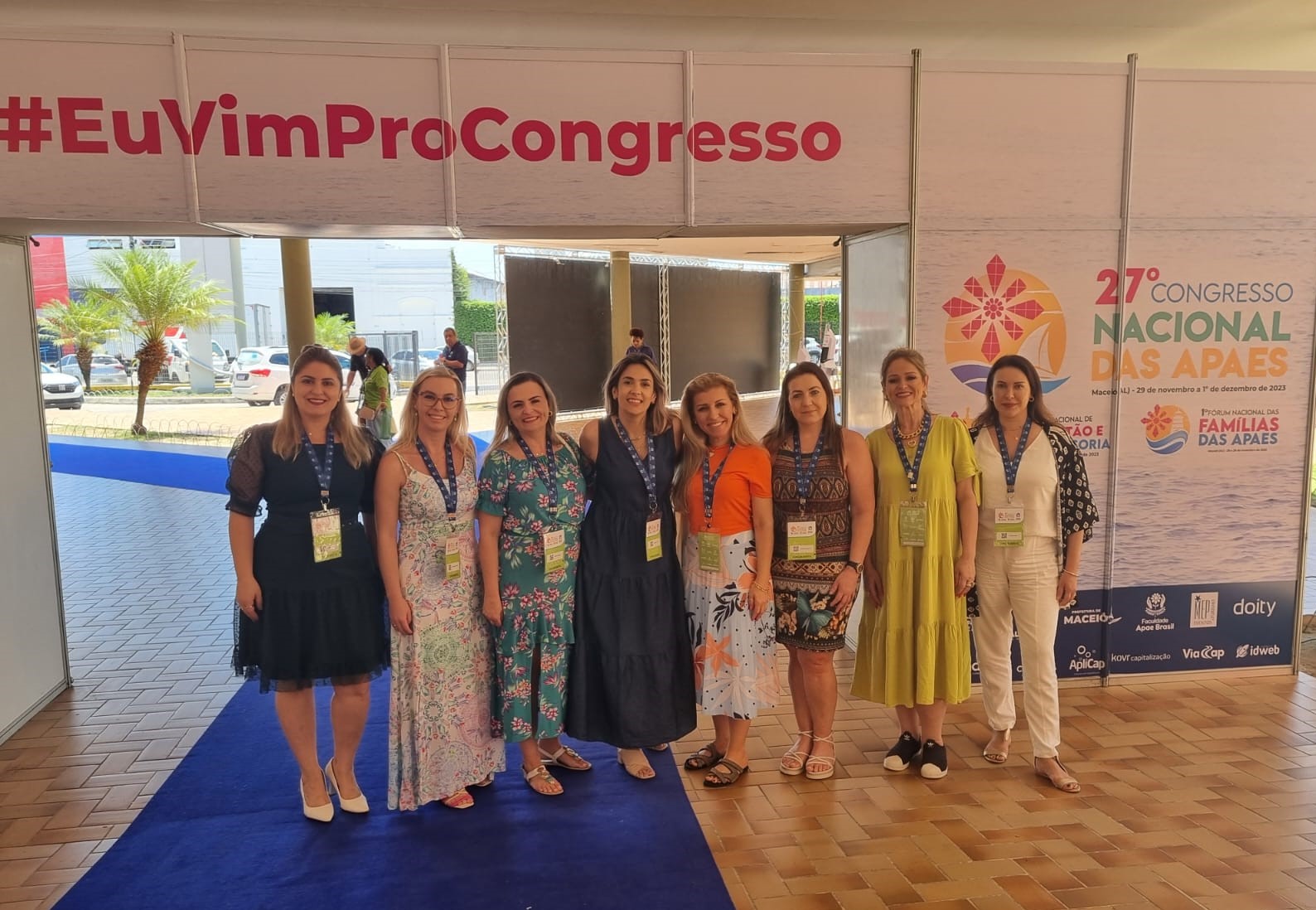 Imagem de 8 mulheres em pé posando para foto, ambiente interno, tapete azul, ao fundo letreiro #euvimprocongresso 27º congresso nacional das apaes
