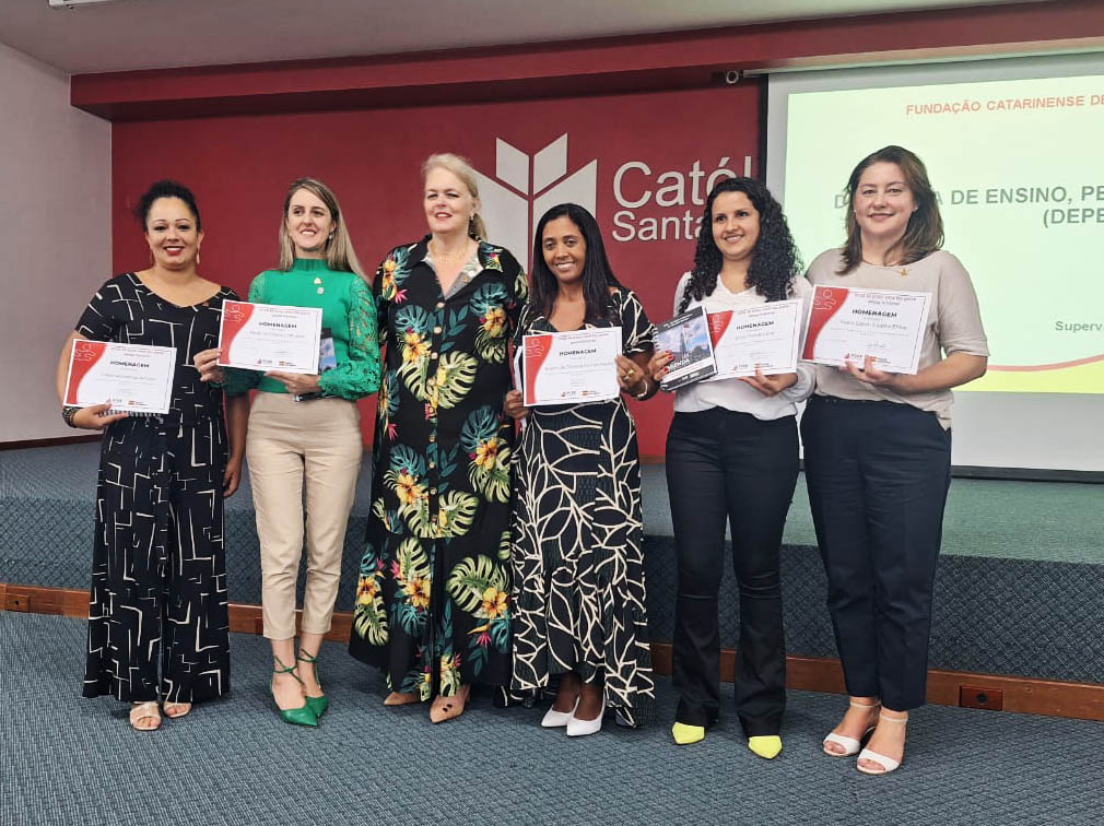 Seis mulheres em pé posam para foto, segurando certificados, ambiente interno