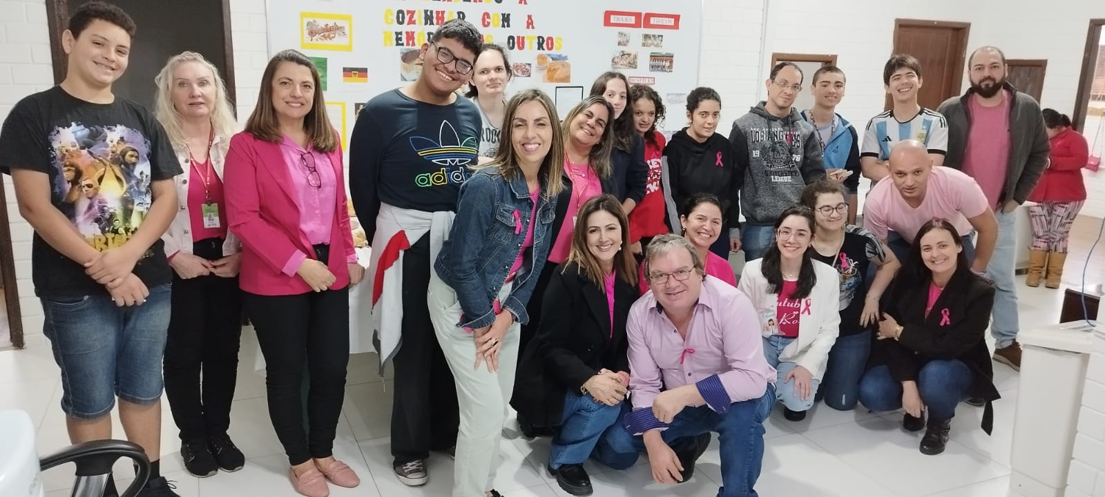 Um grupo de 18 pessoas posam para uma foto em alusão ao outubro rosa. Na foto há professores e alunos, a maioria vestindo blusas rosas em alusão a campanha