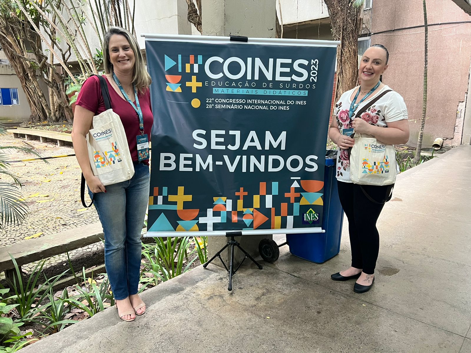 duas pessoas posam para foto ao lado de placa escrito '