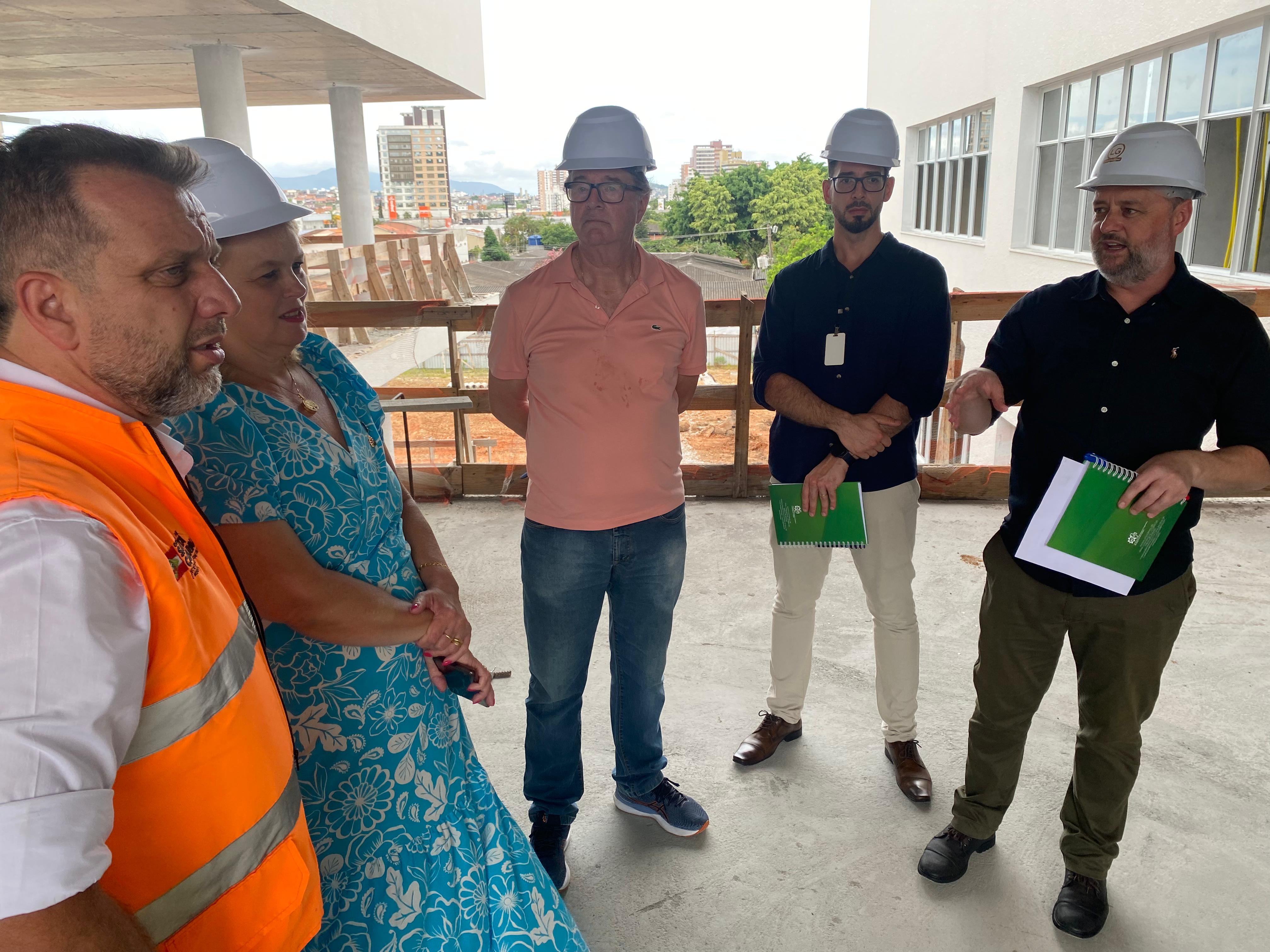 cinco pessoas em pé, com capacetes de proteção, conversam dentro de obra