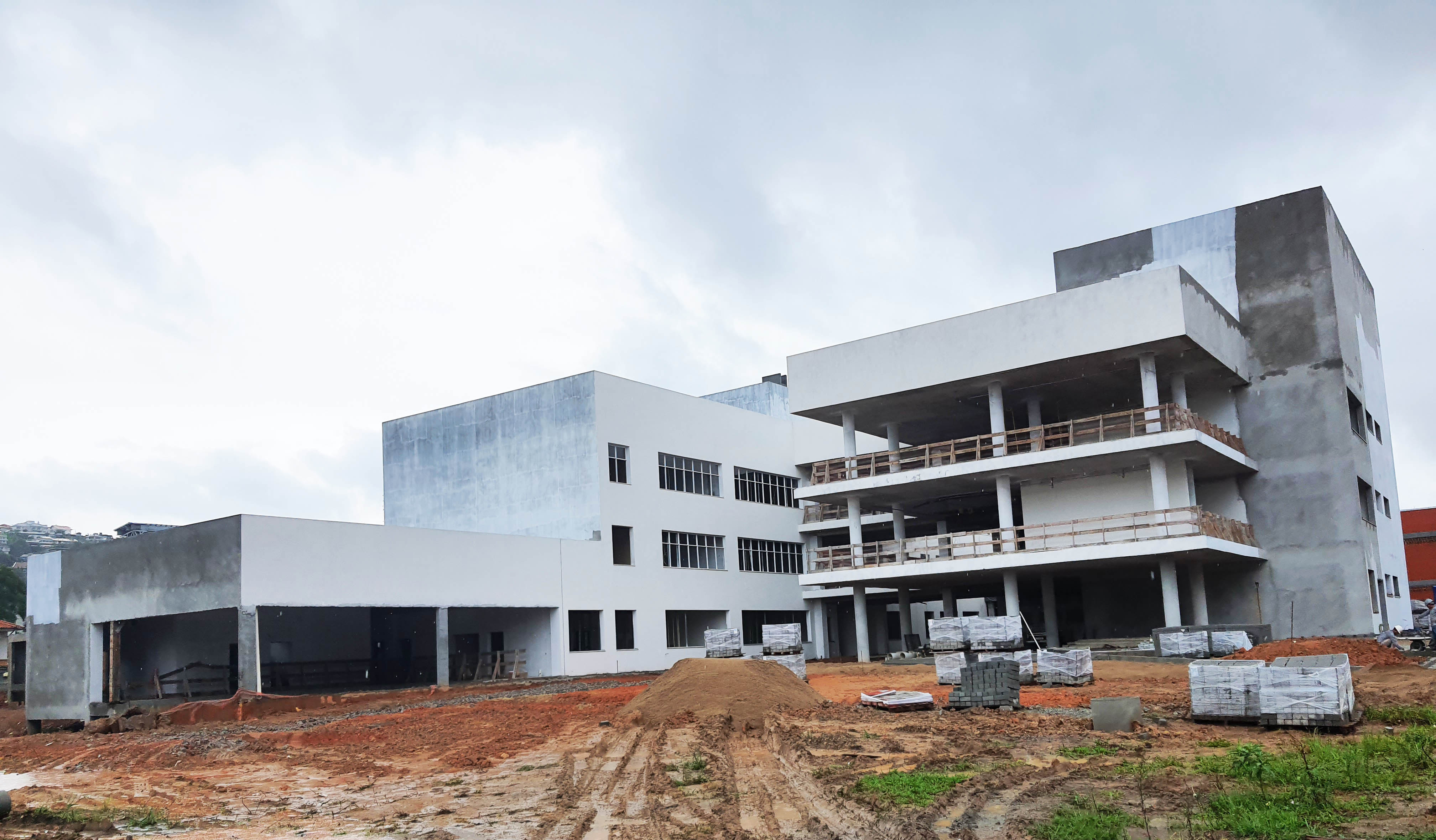 Edifício de 3 andares em obra, pintado parcialmente de branco, terra no chão