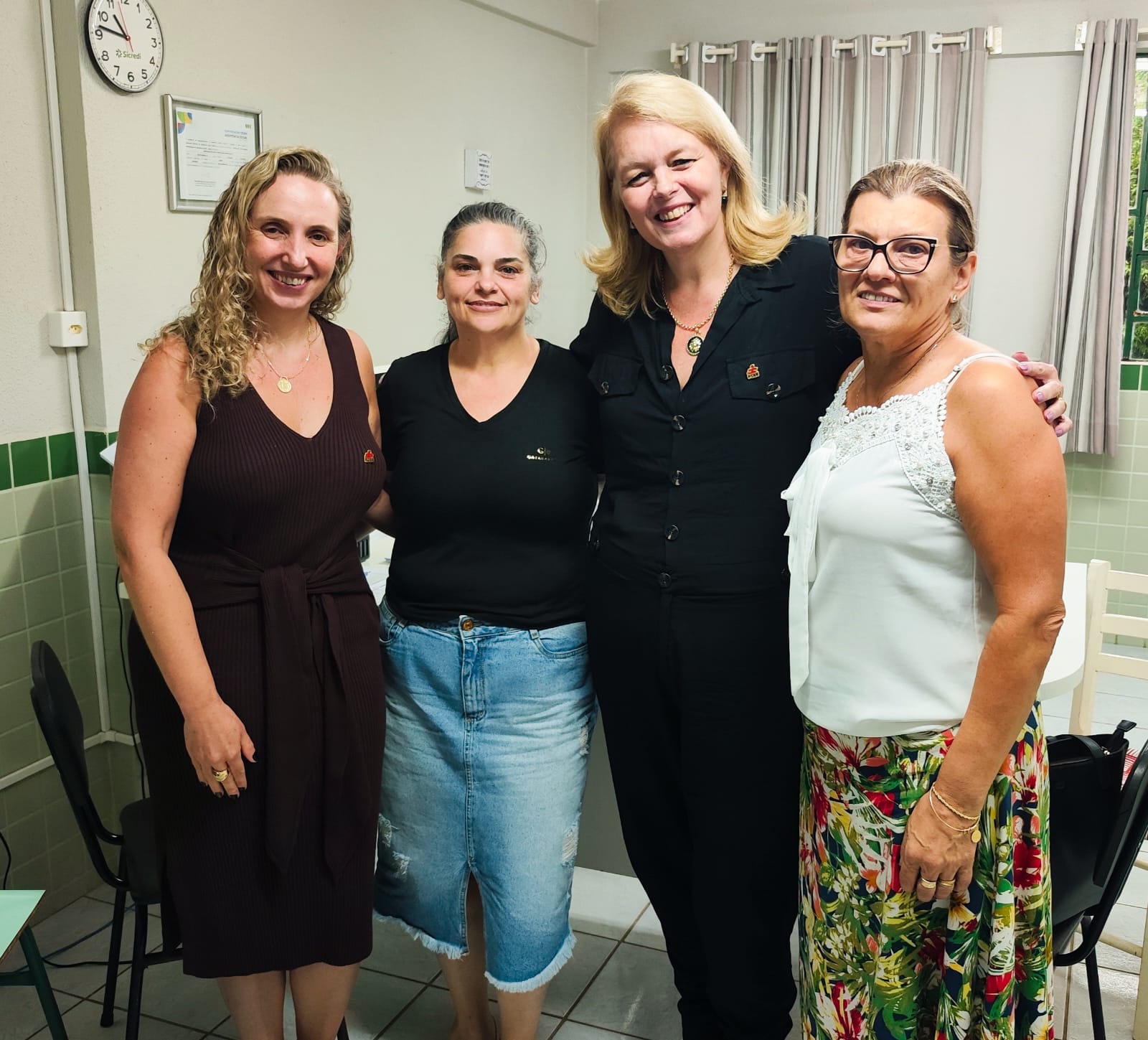 Ambiente interno, 4 mulheres em pé posam para foto sorrindo